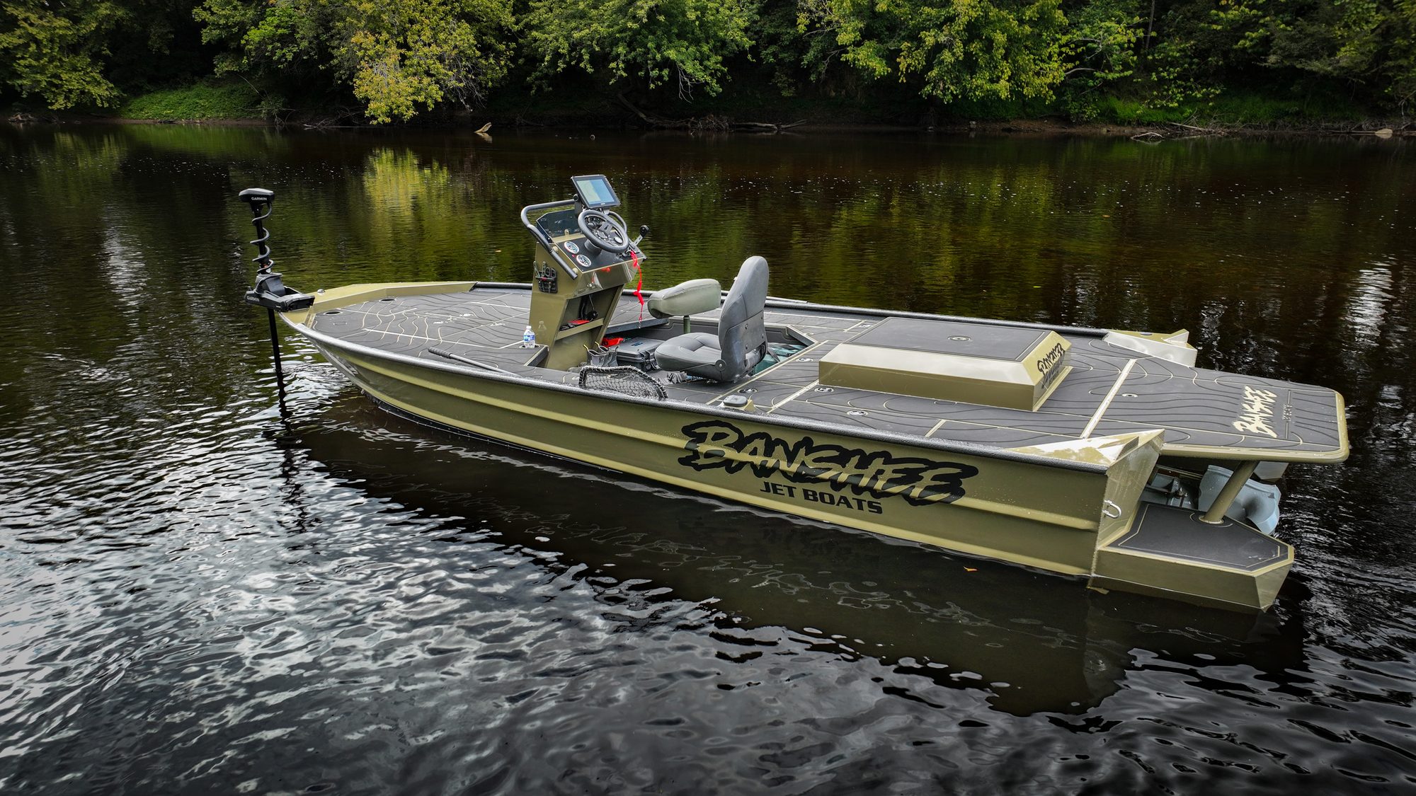 A green Banshee jet boat at rest on a calm, tree-lined river
